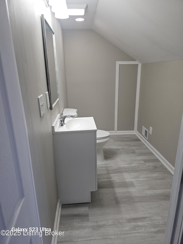 half bath with visible vents, toilet, vaulted ceiling, vanity, and wood finished floors