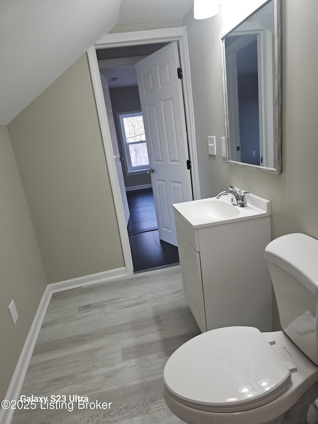 half bath with toilet, baseboards, vaulted ceiling, and wood finished floors