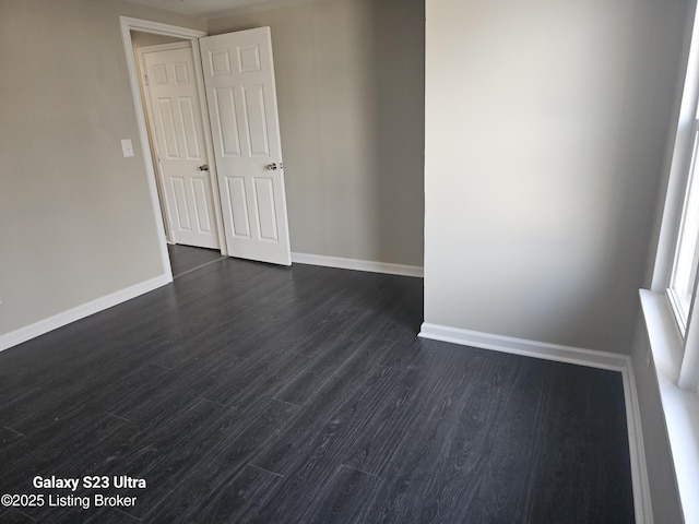 unfurnished room with dark wood-type flooring and baseboards