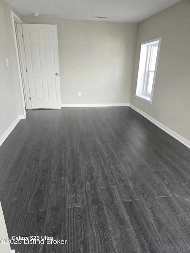 empty room with dark wood-style floors, visible vents, and baseboards