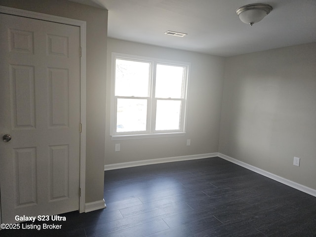 unfurnished room featuring dark wood-style floors, visible vents, and baseboards