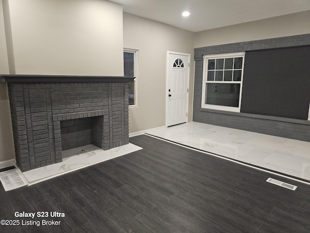 unfurnished living room with a brick fireplace, visible vents, baseboards, and wood finished floors