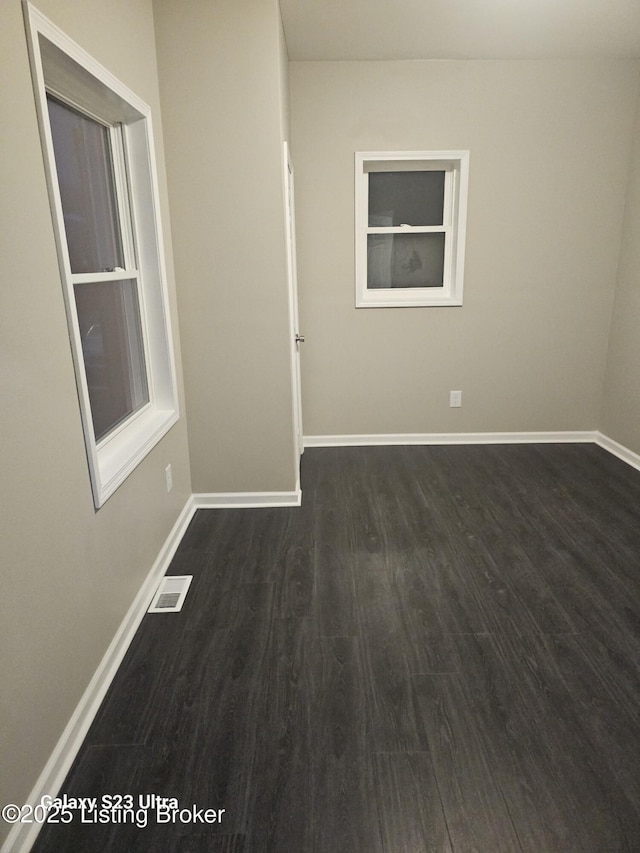 unfurnished room featuring dark wood-style floors, visible vents, and baseboards