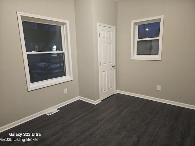 spare room with dark wood-style floors, visible vents, and baseboards