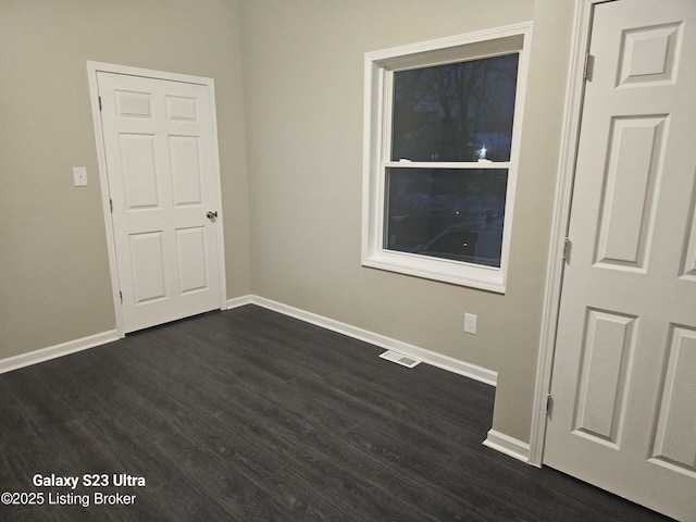 unfurnished room featuring dark wood-style floors, visible vents, and baseboards