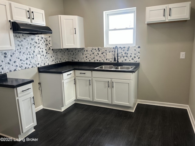 kitchen with dark countertops, white cabinetry, a sink, and under cabinet range hood