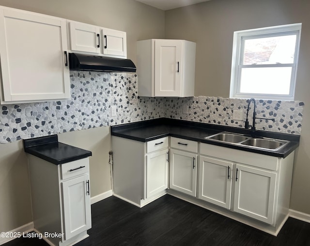 kitchen with tasteful backsplash, white cabinets, dark countertops, under cabinet range hood, and a sink