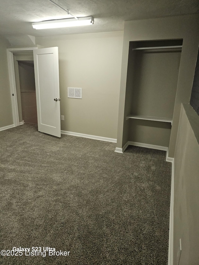 unfurnished bedroom featuring visible vents, a textured ceiling, dark carpet, and baseboards