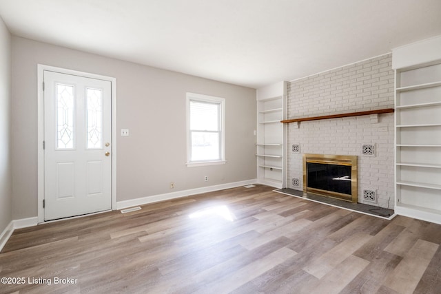 unfurnished living room featuring a brick fireplace, wood finished floors, and baseboards