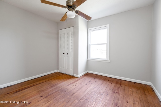 unfurnished bedroom featuring hardwood / wood-style floors, baseboards, a closet, and a ceiling fan