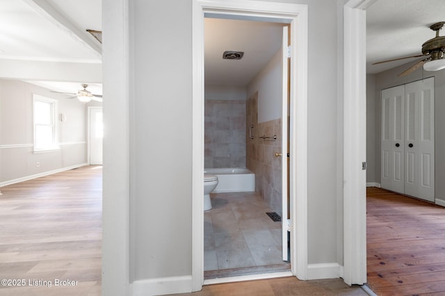 hall with tile walls, wood finished floors, visible vents, and baseboards