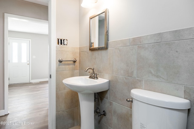 half bath featuring tile walls, toilet, wood finished floors, and a sink