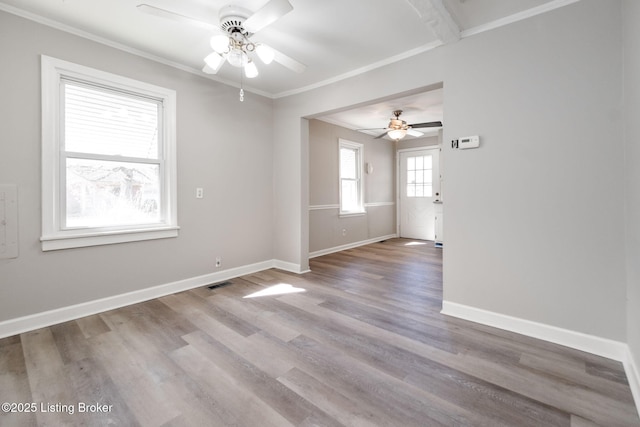 empty room with ceiling fan, wood finished floors, baseboards, and ornamental molding