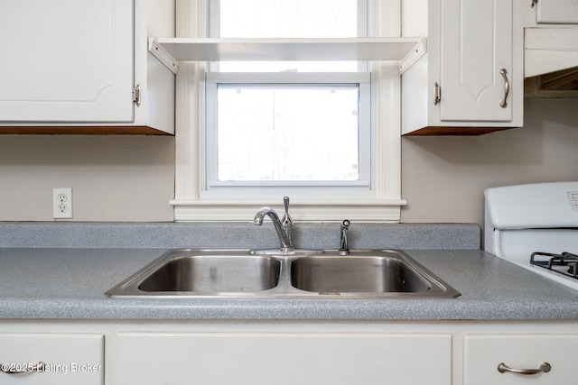 kitchen with white gas stove, white cabinets, and a sink