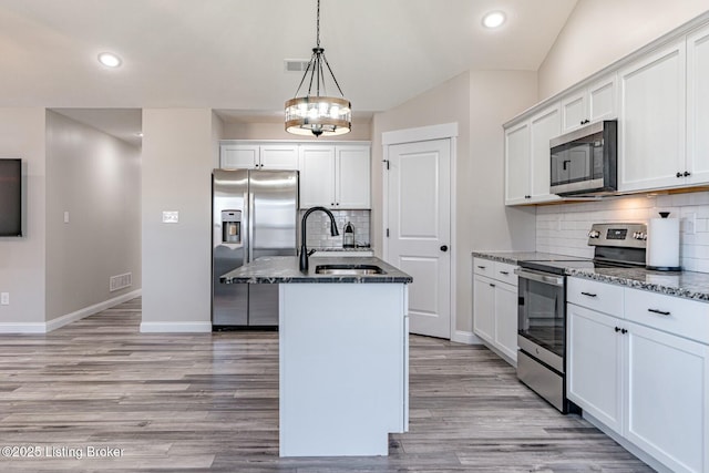 kitchen featuring appliances with stainless steel finishes, dark stone countertops, a sink, and visible vents