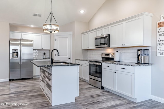 kitchen featuring a sink, visible vents, vaulted ceiling, appliances with stainless steel finishes, and dark stone countertops