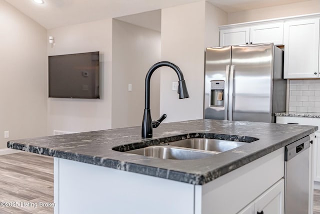 kitchen with light wood-style flooring, white cabinets, appliances with stainless steel finishes, tasteful backsplash, and a center island with sink