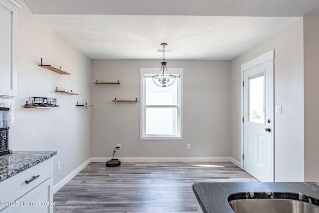 kitchen featuring wood finished floors, white cabinets, a textured ceiling, light stone countertops, and baseboards