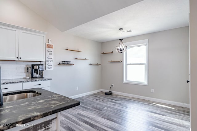 kitchen with white cabinetry, baseboards, light wood-type flooring, dark stone counters, and tasteful backsplash