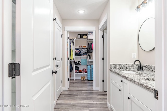 bathroom with a textured ceiling, a walk in closet, wood finished floors, and vanity