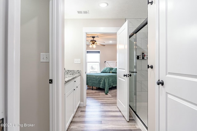 ensuite bathroom with a shower stall, connected bathroom, visible vents, and wood finished floors