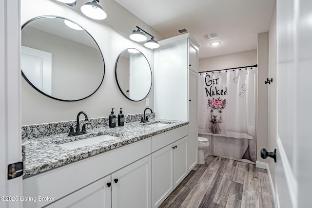 bathroom with toilet, visible vents, a sink, and wood finished floors