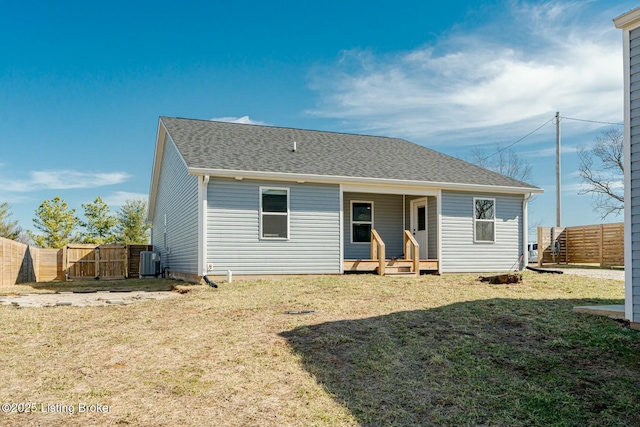 back of property with central AC unit, covered porch, fence, a yard, and roof with shingles