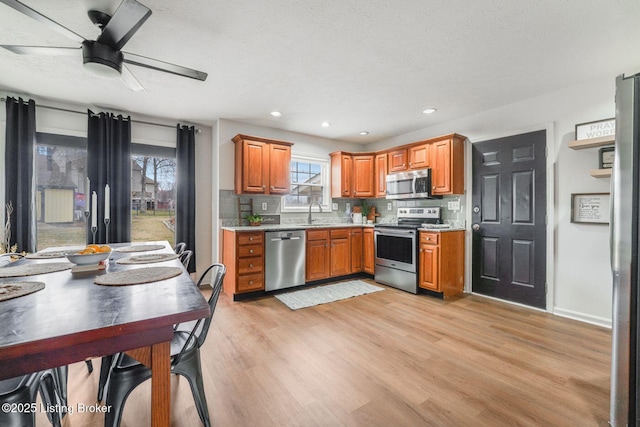 kitchen featuring stainless steel appliances, light countertops, backsplash, brown cabinetry, and light wood-type flooring