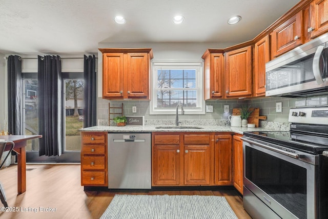 kitchen featuring wood finished floors, decorative backsplash, appliances with stainless steel finishes, a sink, and light stone countertops