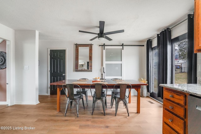 dining area with a ceiling fan, a textured ceiling, light wood finished floors, and a barn door