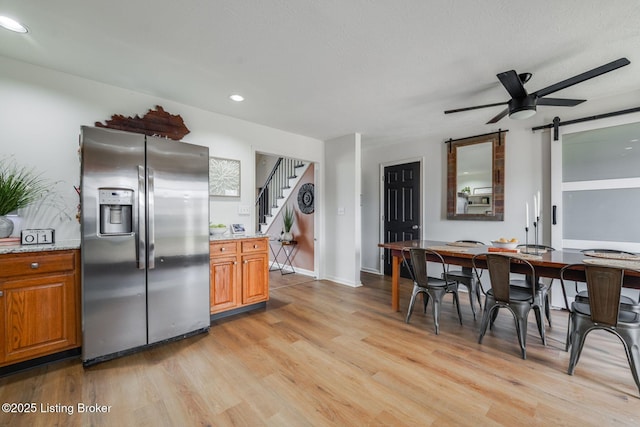 kitchen with a barn door, stainless steel fridge with ice dispenser, ceiling fan, brown cabinets, and light wood-style floors