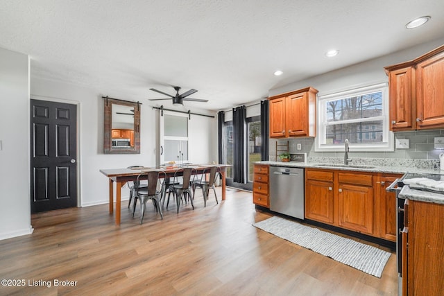 kitchen featuring light wood finished floors, decorative backsplash, a barn door, appliances with stainless steel finishes, and a sink