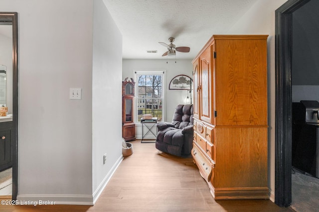 interior space featuring light wood finished floors, visible vents, a ceiling fan, a textured ceiling, and baseboards