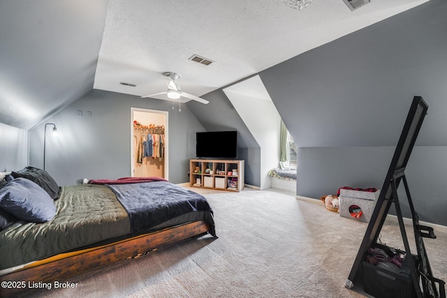 carpeted bedroom with baseboards, visible vents, a walk in closet, vaulted ceiling, and a textured ceiling