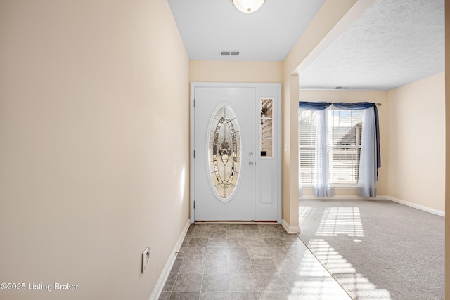 carpeted entryway featuring a textured ceiling, visible vents, and baseboards