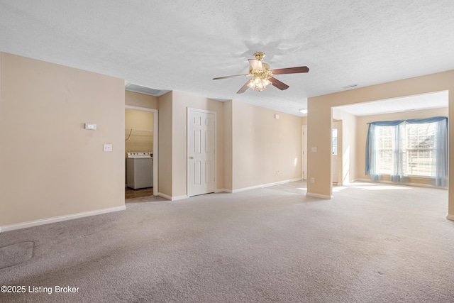 unfurnished room featuring a textured ceiling, light carpet, a ceiling fan, baseboards, and washer / dryer