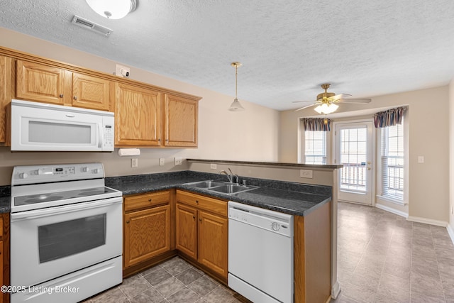 kitchen with white appliances, visible vents, dark countertops, a peninsula, and a sink