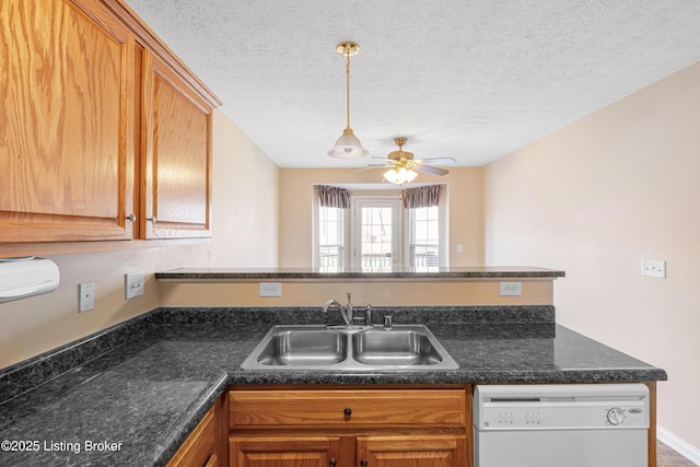 kitchen featuring a ceiling fan, dark countertops, a peninsula, white dishwasher, and a sink