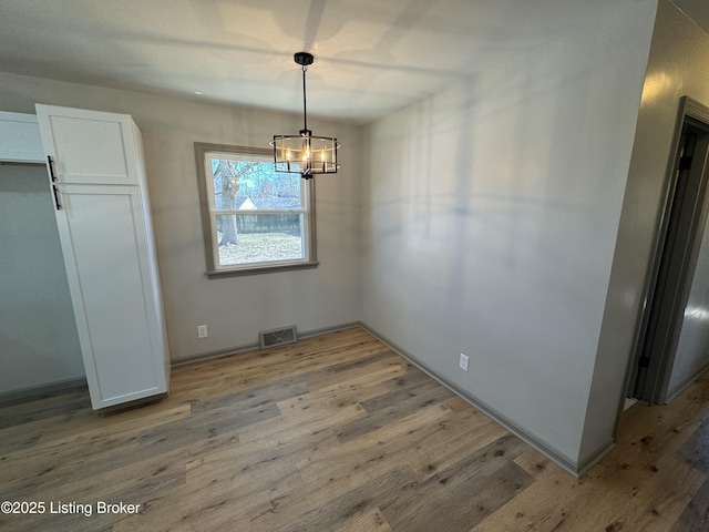 unfurnished dining area with light wood finished floors, visible vents, a chandelier, and baseboards