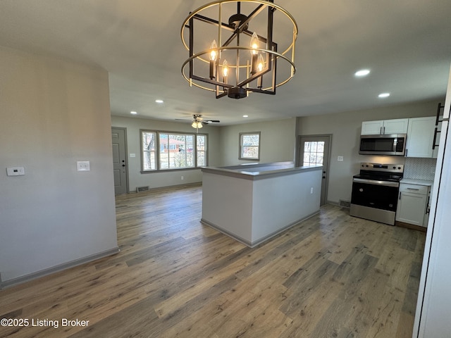 kitchen featuring a wealth of natural light, appliances with stainless steel finishes, open floor plan, white cabinetry, and wood finished floors