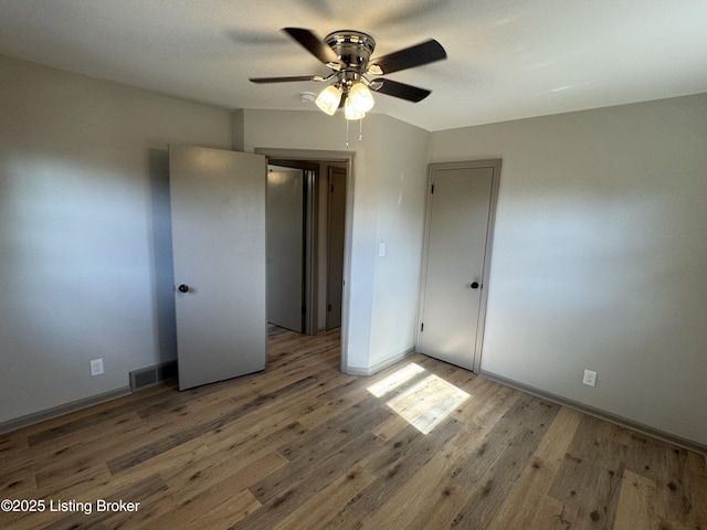 unfurnished bedroom featuring a ceiling fan, wood finished floors, visible vents, and baseboards