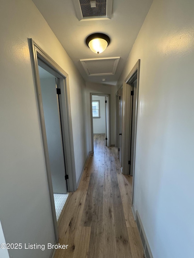 hall with baseboards, light wood-style floors, visible vents, and attic access