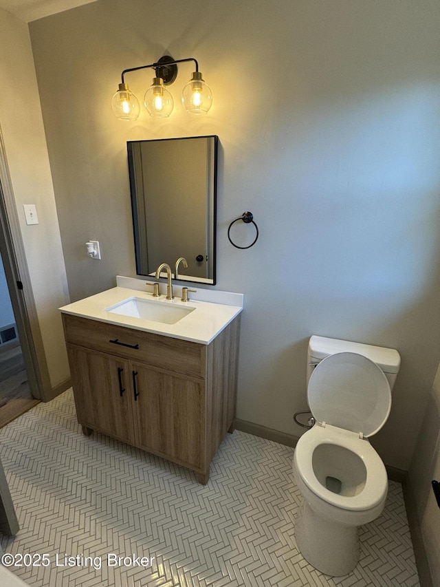 half bathroom featuring toilet, vanity, baseboards, and tile patterned floors