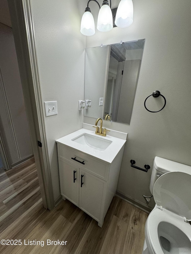 half bath with baseboards, vanity, toilet, and wood finished floors