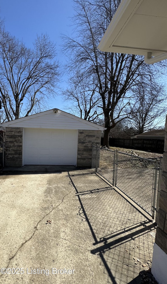 detached garage featuring driveway, fence, and a gate