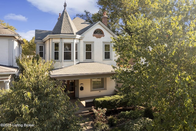 victorian-style house featuring covered porch, roof with shingles, and a chimney