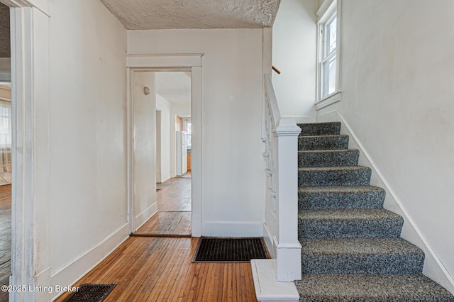 stairway with baseboards, a healthy amount of sunlight, a textured ceiling, and hardwood / wood-style floors