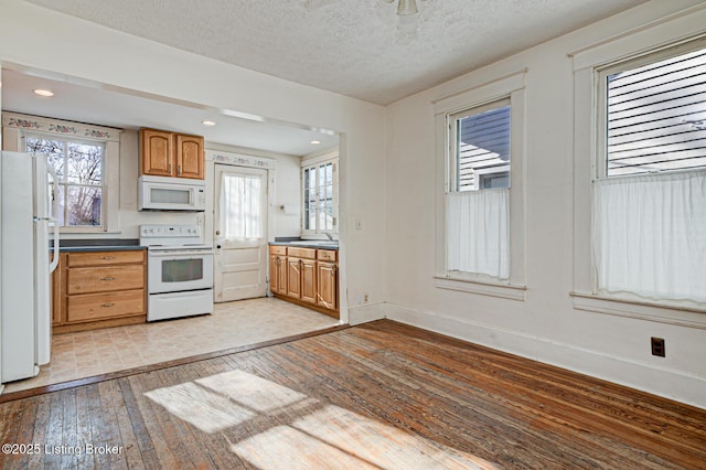 kitchen with white appliances, baseboards, light wood-style floors, brown cabinetry, and dark countertops