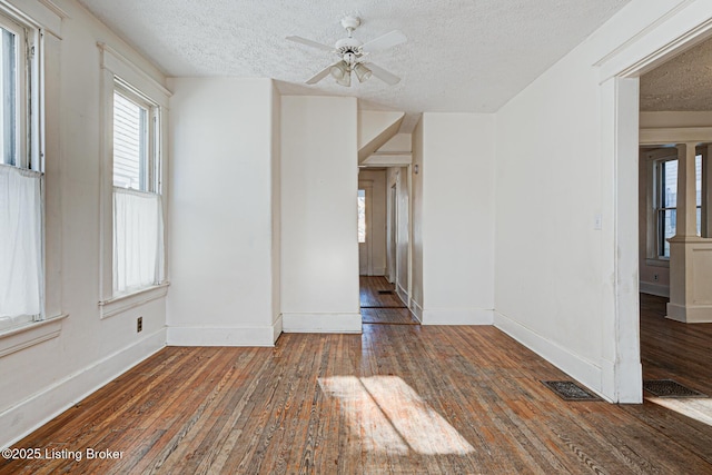 unfurnished room with a textured ceiling, a ceiling fan, visible vents, baseboards, and wood-type flooring