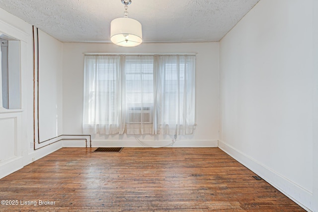 empty room with dark wood-type flooring, visible vents, a textured ceiling, and baseboards